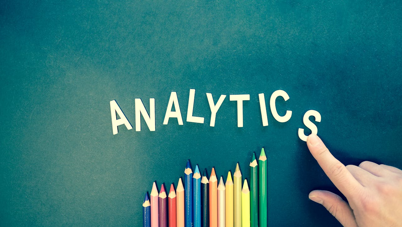 services-01 Colored pencils and letters spelling 'ANALYTICS' on a textured background with a hand.