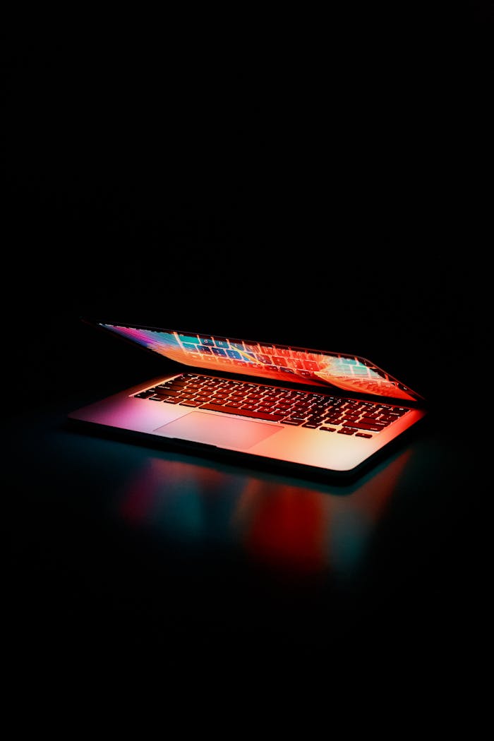 services-03 Laptop partially opened, emitting vibrant multicolored lights in dark setting.